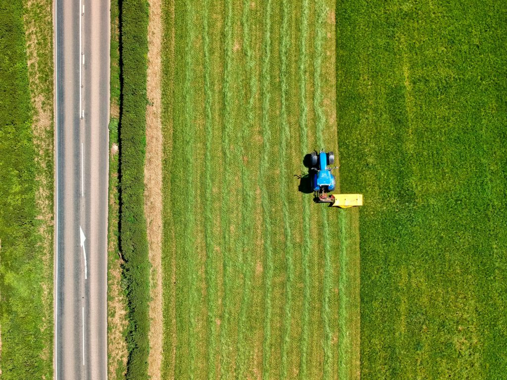 Image of a blue tractor in a green field parallel to a paved road.